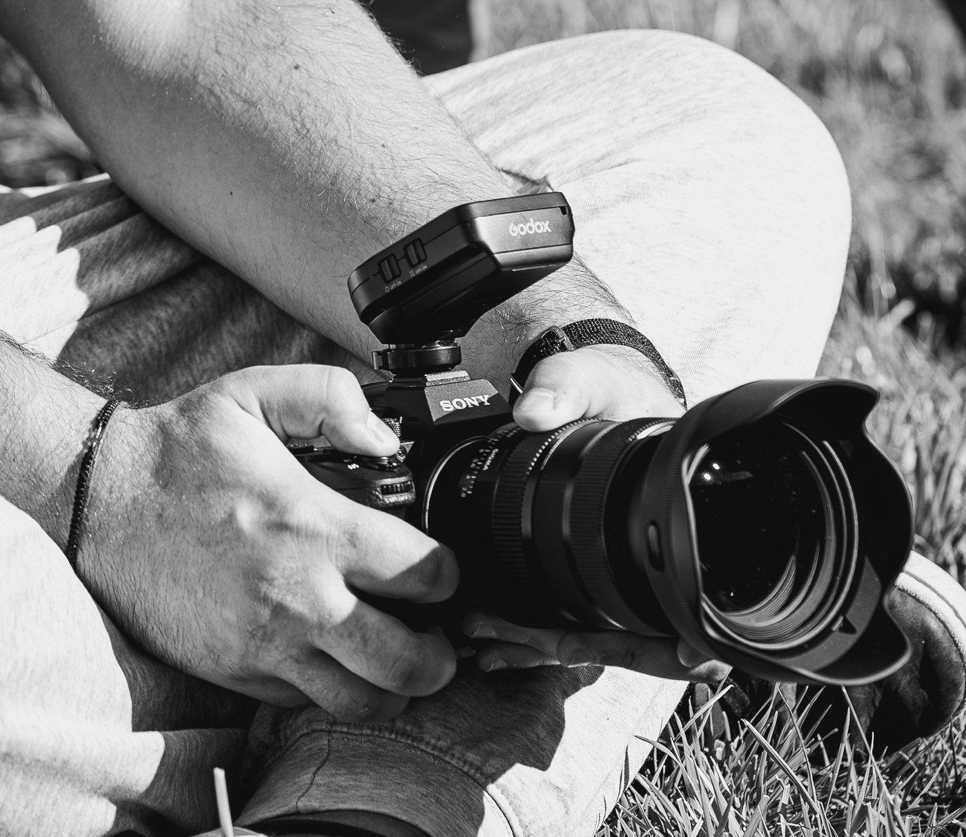 Las manos de un fotógrafo, sentado en la hierba, sostienen una cámara con un disparador de flash