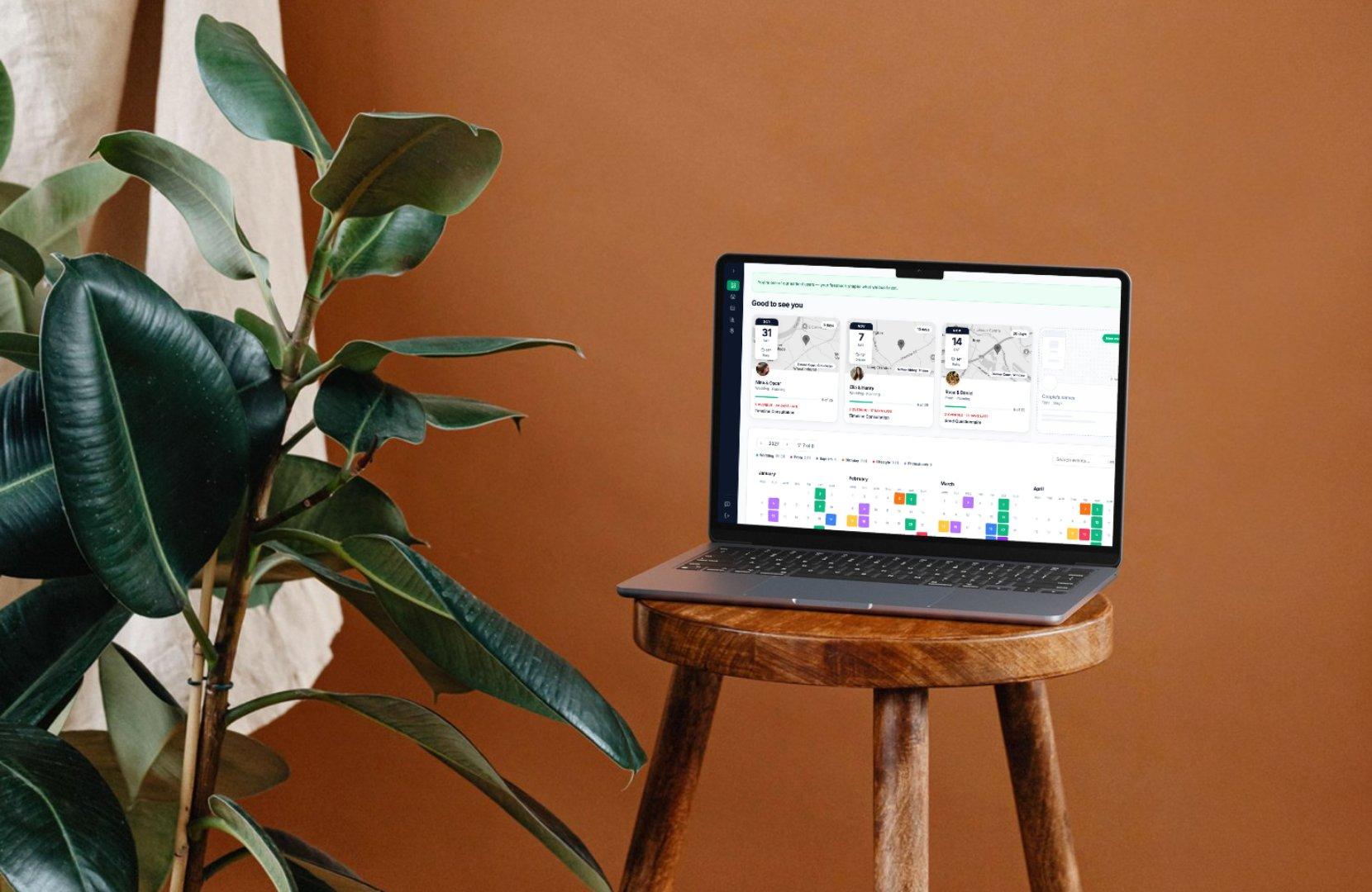 Un portátil sobre un taburete de madera frente a una pared terracota, con una planta al lado, mostrando el panel de WeddingRunbook