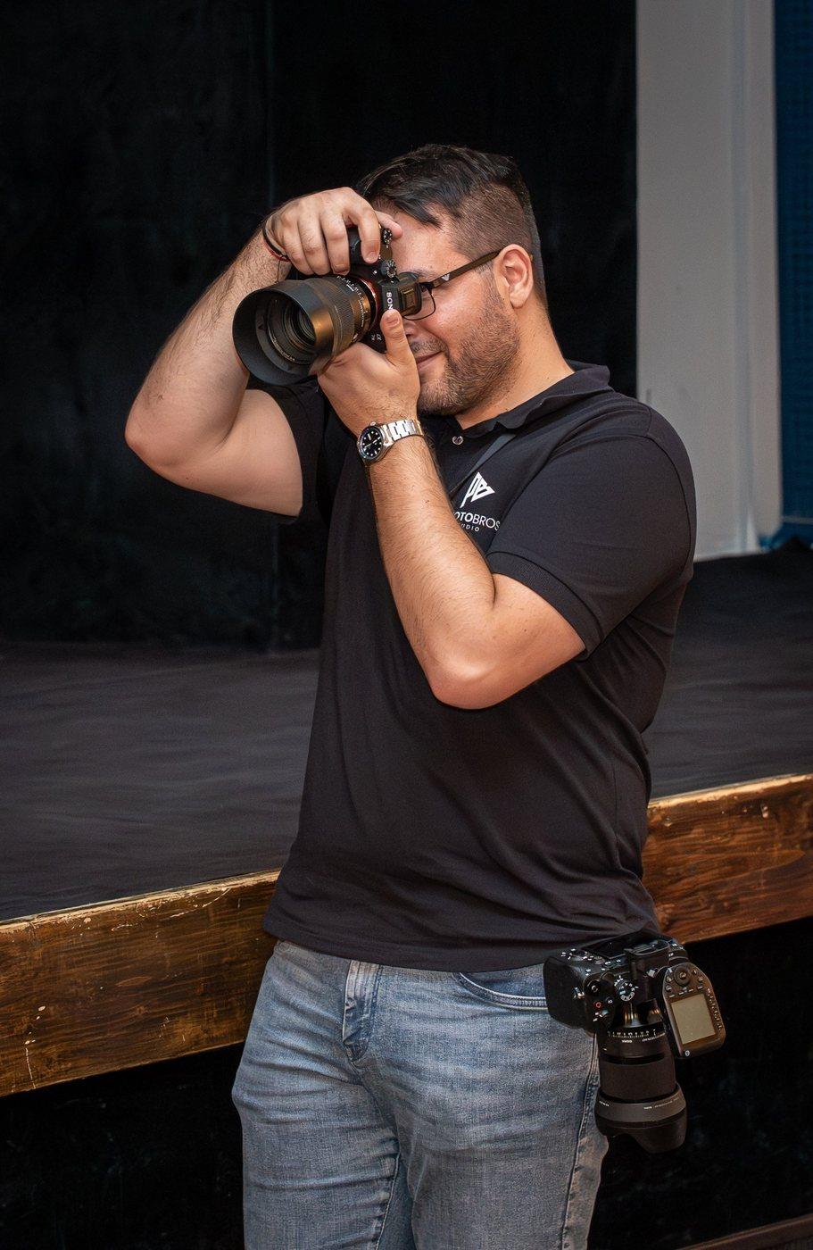 Ilko con el polo de PhotoBros, el ojo en el visor y una segunda cámara en la cadera