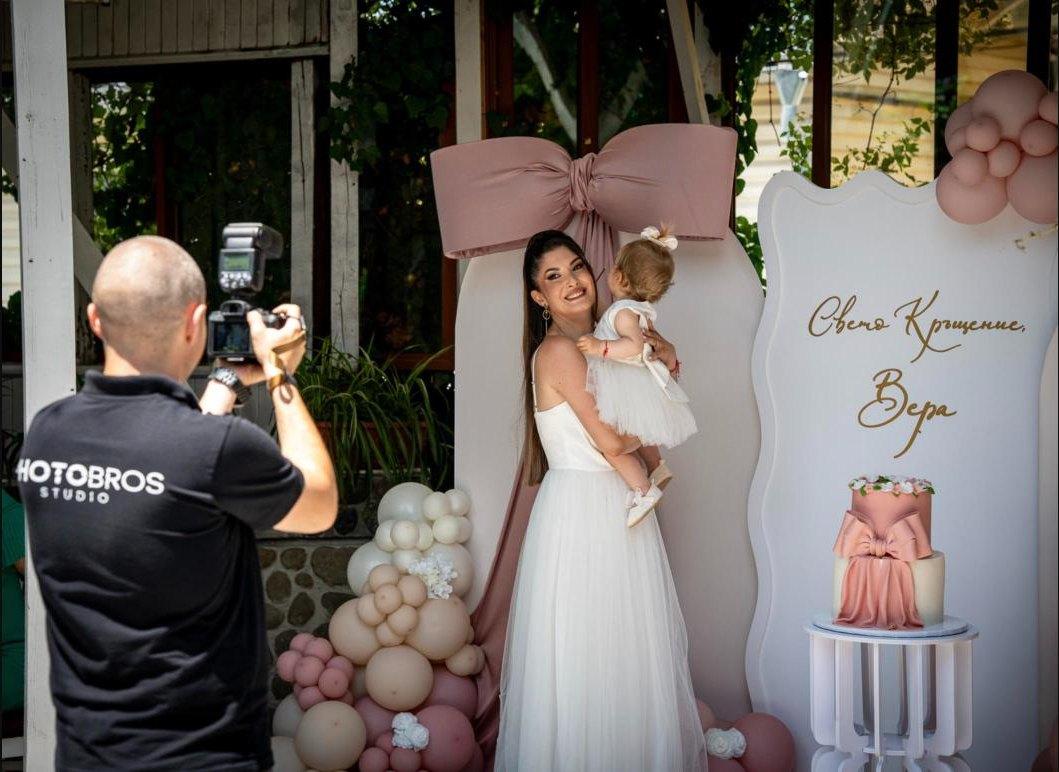 Un fotógrafo de PhotoBros, con el polo negro del estudio, fotografiando a una madre con su hija en un bautizo