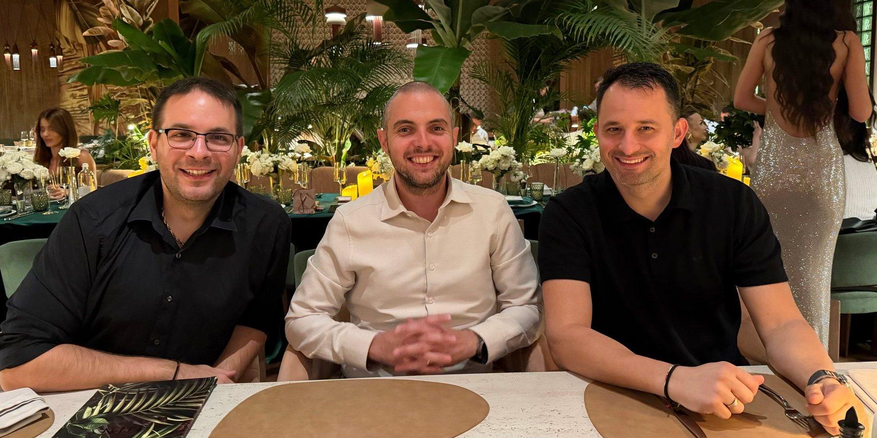 Ilko, Atanas y Rado en una mesa larga de un restaurante lleno de plantas, sonriendo a la cámara